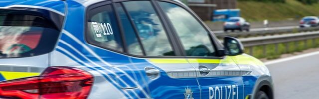 Seitenansicht eines fahrenden blauen Polizeiautos mit neongelber und blauer Markierung auf Autobahn