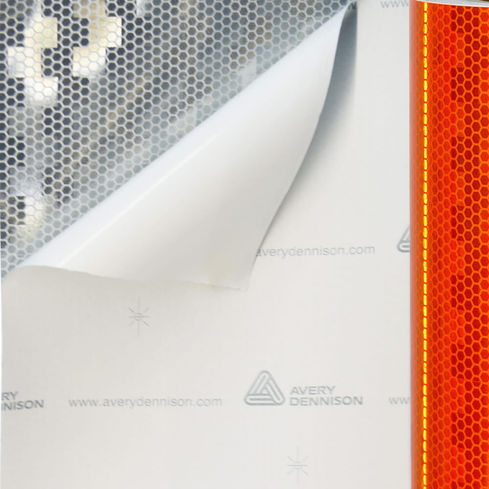 Abgelöste Ecke zeigt silbernen Klebstoffträger unter fluor-orangen Avery V-8000 Reflexfolie