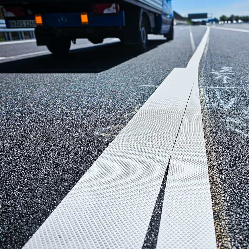 Zwei aneinanderstoßende Streifen weißer Markierungsfolie auf Asphalt