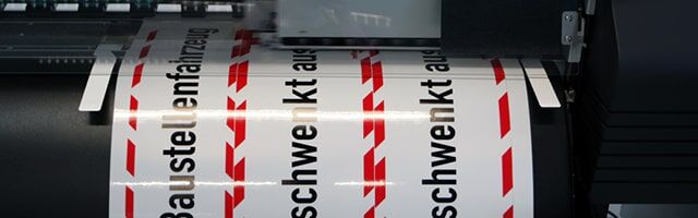 Eine Rolle mit weißen Aufklebern und rot-weißen Warnstreifen am Rand in einem Drucker.