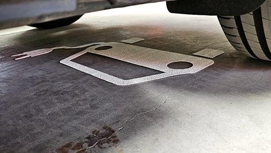 Abschnittstitelbild zu Piktogrammen für Parkplätze Das Bild zeigt ein E-Auto Piktogramm auf einer Parkplatzfläche mit darüber Parkendem Auto aus Bodenperspektive