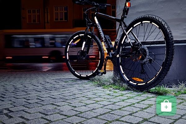 Ein schwarzes Mountainbike mit reflektierenden Felgenaufklebern steht in der Dämmerung auf gepflastertem Boden.