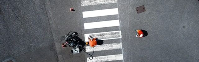 Vogelperspektive auf Personen in Warnschutzkleidung, die einen Zebrastreifen auf die Fahrbahn aufbringen