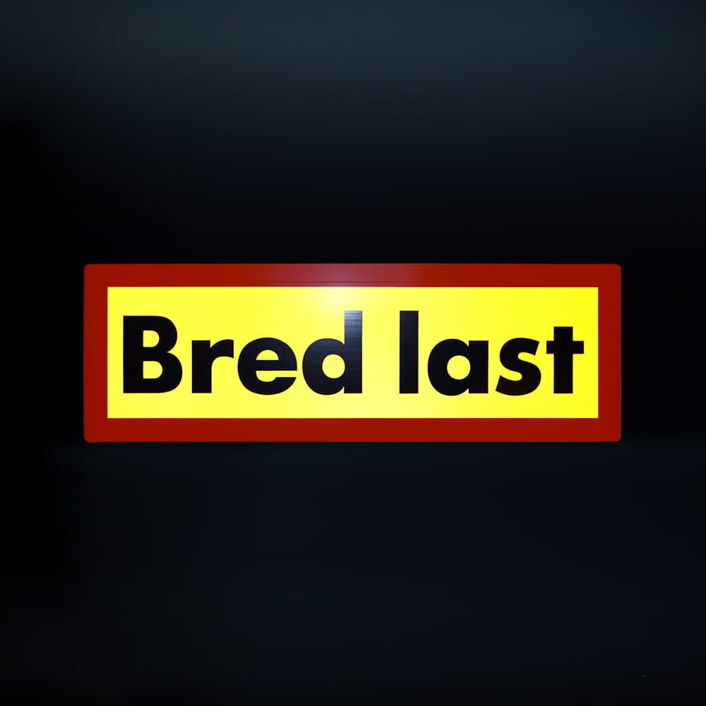 Reflektierende „Bred last“-Tafel leuchtet bei Nacht auf schwarzem Hintergrund