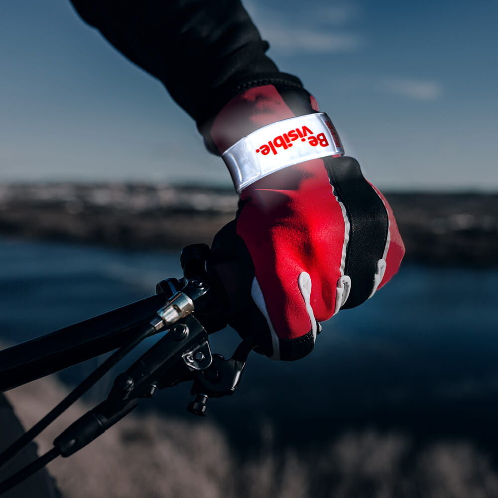 Radfahrerhand mit weißem reflektierendem Schnapparmband „Be visible.“ am Handgelenk