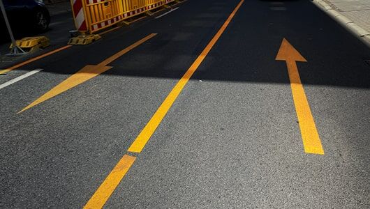 Abschnittstitelbild zu Pfeilen für den städtischen Bereich Das Bild zeigt temporär verlegte Fahrbahnmarkierung zur Änderung der Verkehrsführung an einer Baustelle aus Linienmarkierung und Geradeaus-Pfeilen