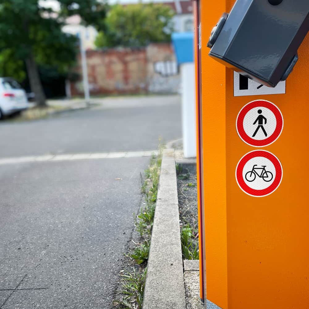 Verbot für Fußgänger-Aufkleber auf oranger Schranke neben Fahrradverbotsschild