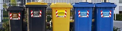 Farbige Mülltonnen mit reflektierenden Aufklebern für Bio-, Rest-, Plastik- und Papierabfall.