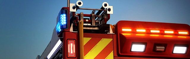 Ein Feuerwehrfahrzeug mit eingeschaltetem Blaulicht und Heckvollmarkierung in rot und fluor-lime steht bereit für den Einsatz.
