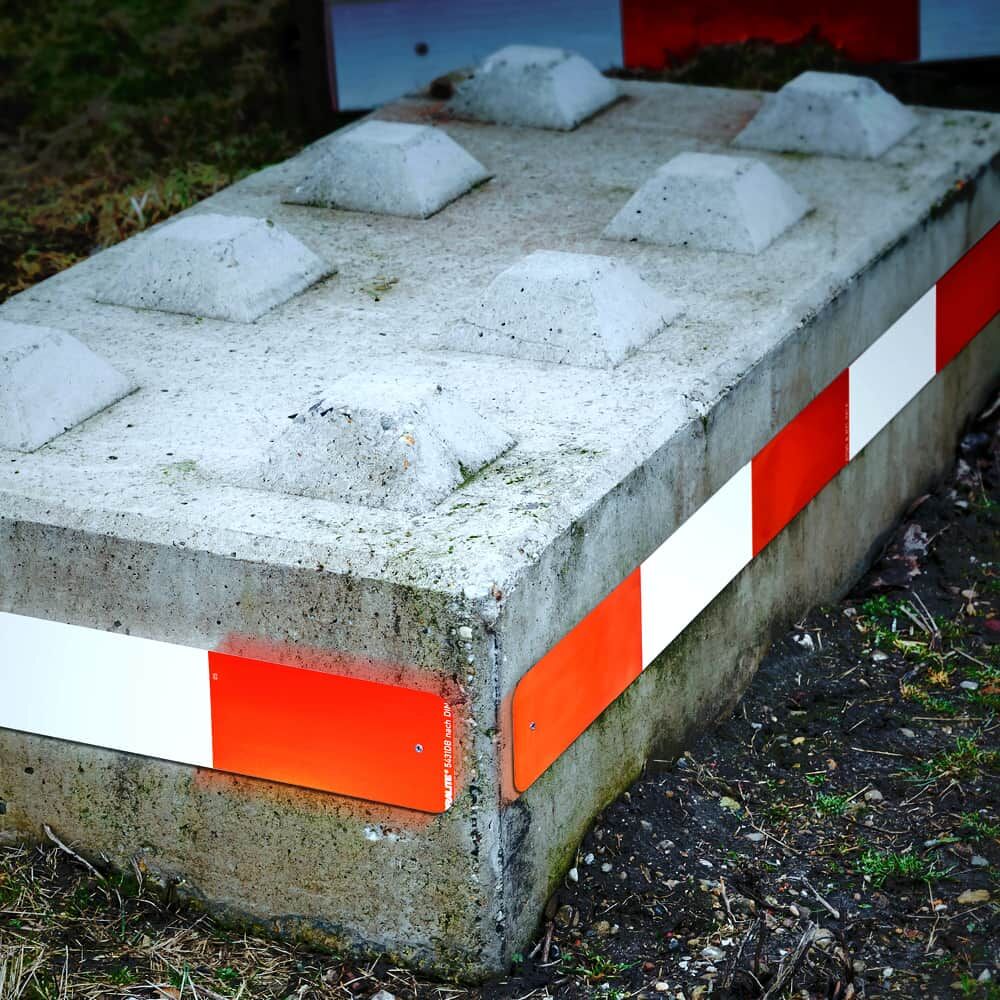 Eckansicht Betonblock mit rot-weißer Warnplatte, zeigt Montage über Eck