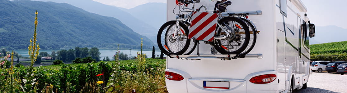 Titelbild Themenseite Caravan Das Titelbild der Themenseite Caravan zeigt ein Wohnmobil mit Fahrradaufspannung und Italientafel auf Landstraße mit See und Bergen im Hintergrund
