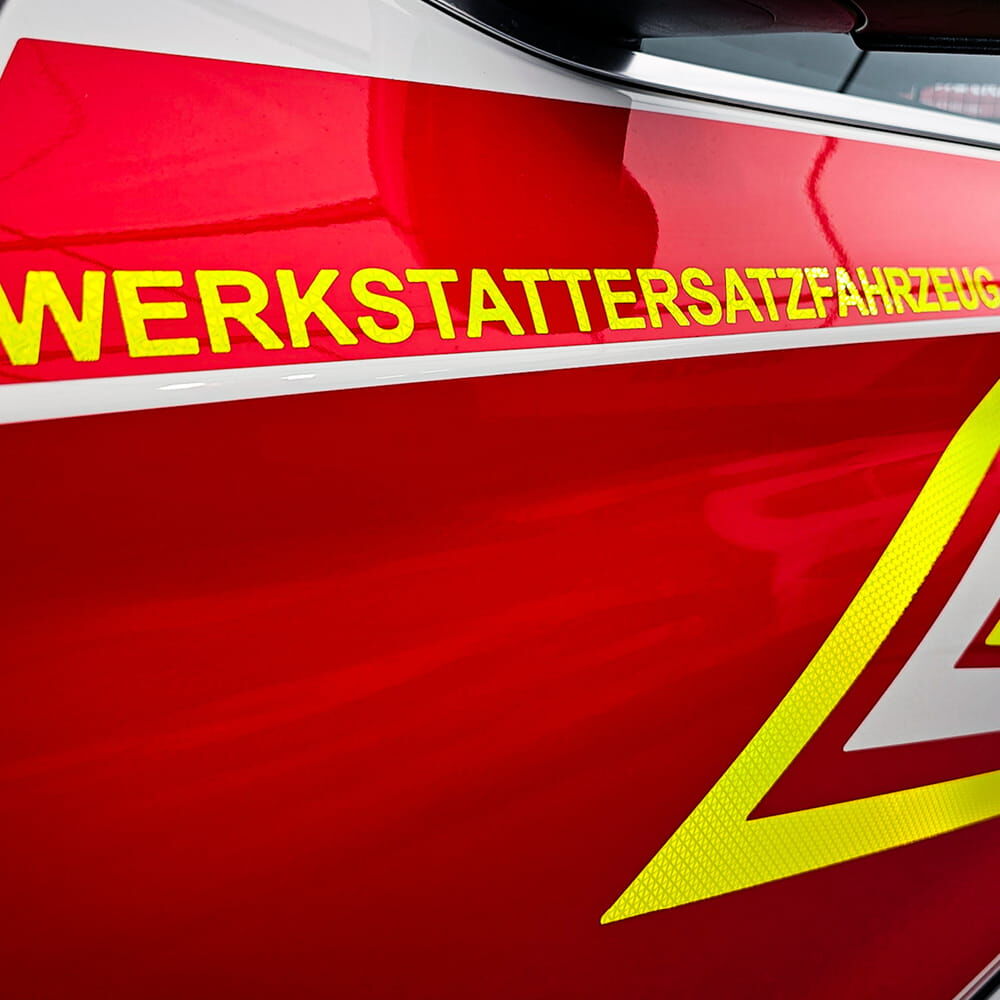 Rote Fahrzeugseite mit gelbem, reflektierendem Schriftzug „WERKSTATTERSATZFAHRZEUG“