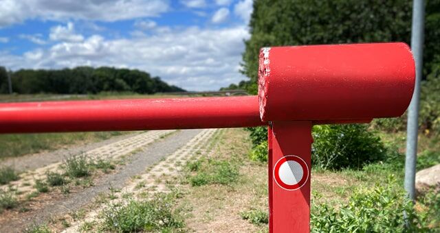 Eine rote Schranke auf einem Feldweg mit einem Durchfahrtsverbotsschild und ländlicher Umgebung.