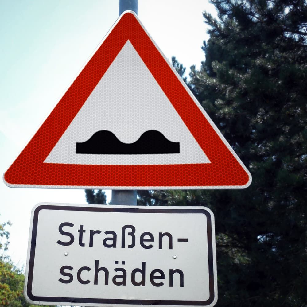 Warnschild Unebene Fahrbahn mit Zusatzschild „Straßenschäden“ am Straßenrand