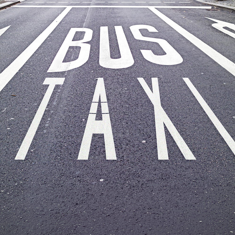 Fahrbahnmarkierung „BUS TAXI“ auf einer Asphaltstraße mit weißen Fahrspumarkierungen