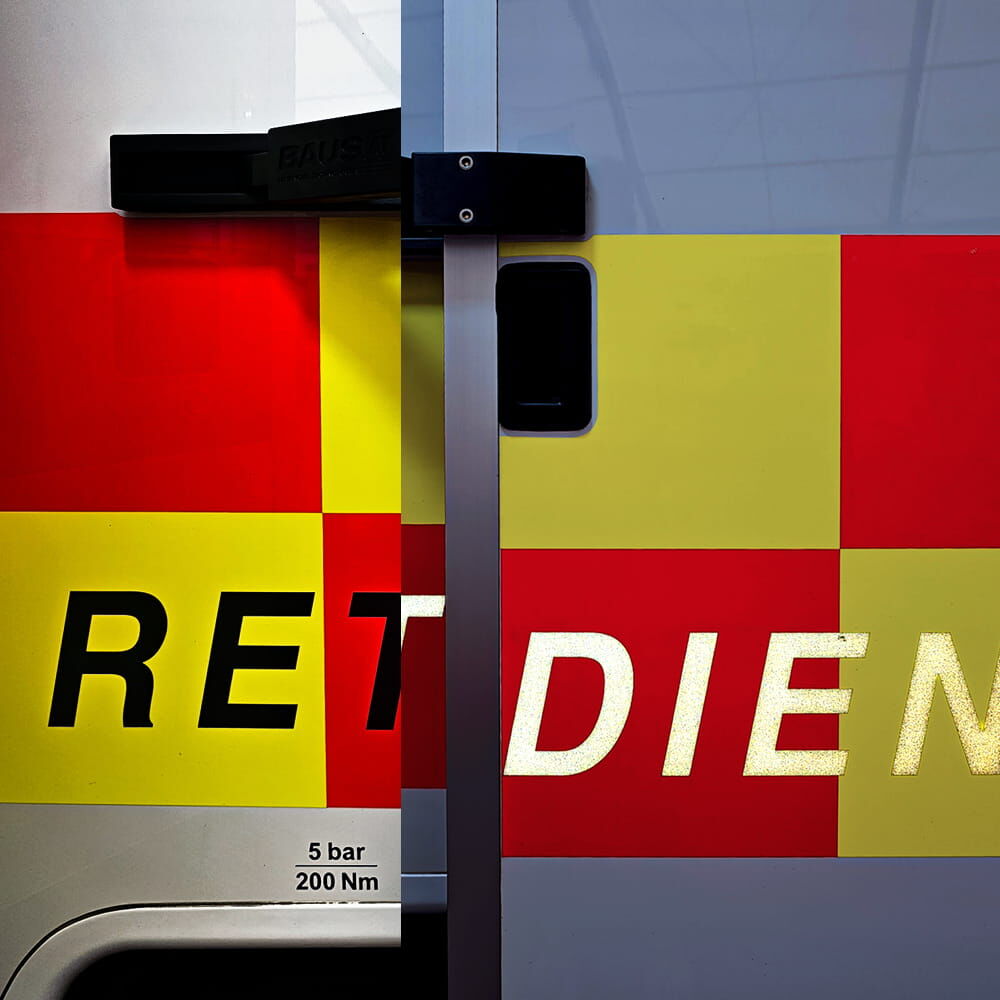 Schwach reflektierende Schrift „DIENST“ auf rot-gelbem Rettungswagen seitlich