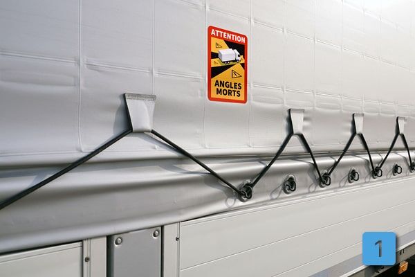 Bild zeigt Detailaufnahme von der Seite eines LKW-Planenaufbaus mit selbstklebendem Angles Morts Schild, speziell für Planenmaterial