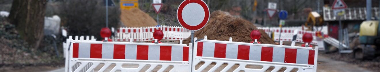 Das Bild zeigt eine Straßensperrung mit rot-weißen Absperrungen, einem Durchfahrtsverbot-Schild und Erdhaufen im Hintergrund.