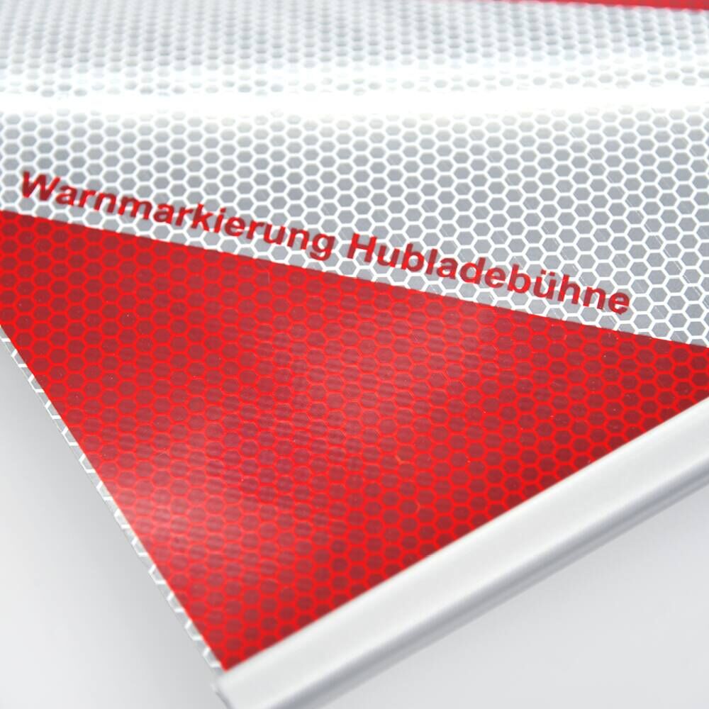 Nahaufnahme mit Aufdruck „Warnmarkierung Hubladebühne“ auf reflektierender Folie