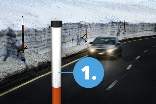 Ein Fahrzeug bewegt sich auf einer geräumten Straße, die mit Snow Sticks markiert ist, umgeben von Schnee an den Seiten. Im Vordergrund die Spitze eines Snow Sticks mit der ORALITE 5930MFlex.