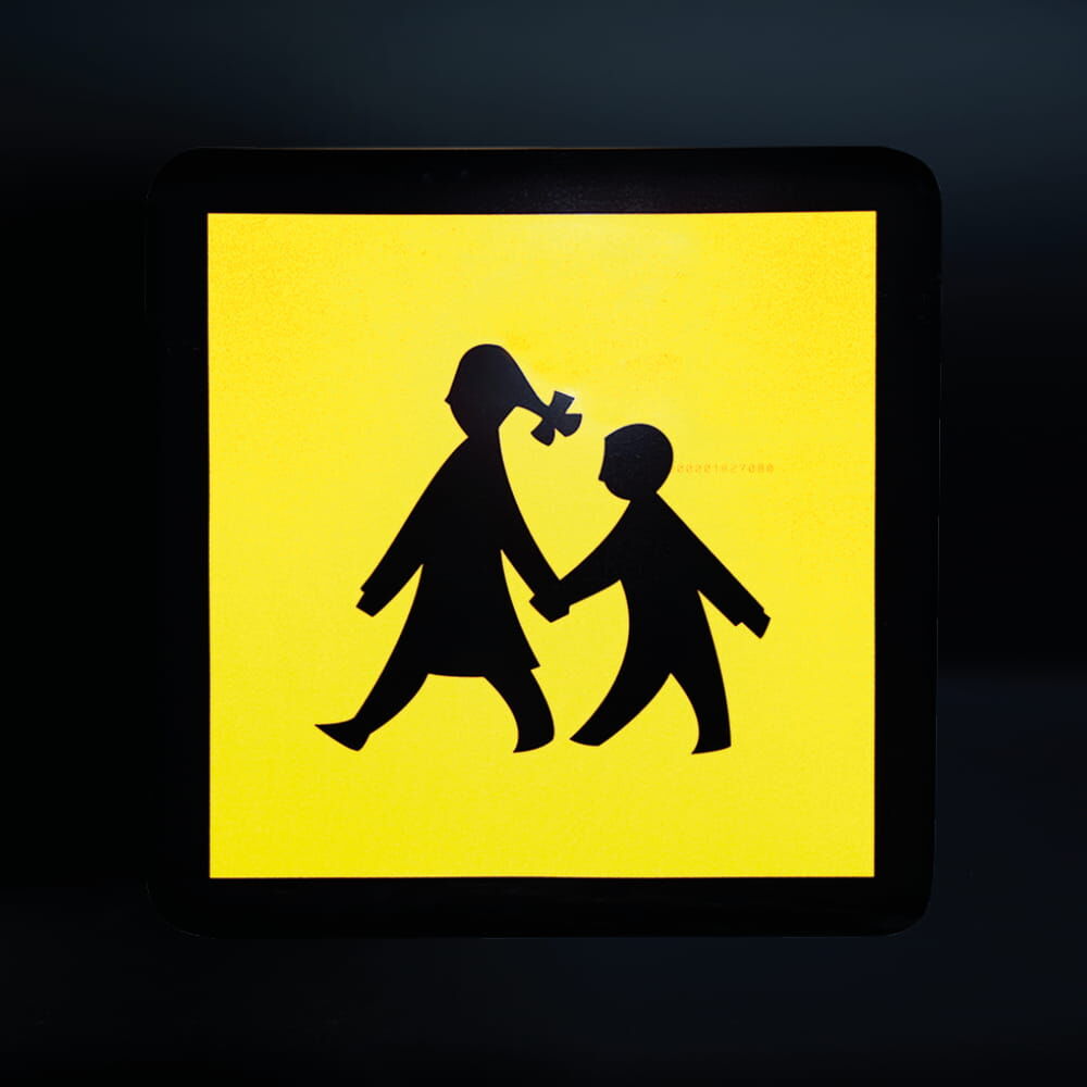 Schild reflektiert gelb im Dunkeln bei Lichteinfall, zeigt Schulkinder-Symbol