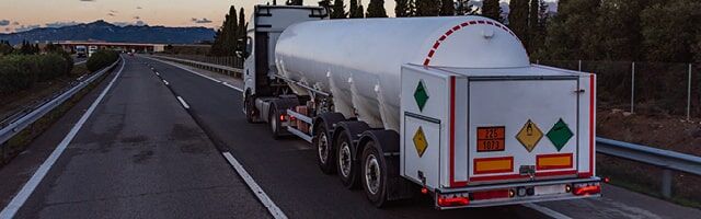 Ein Tanklastzug für Gefahrgut von hinten auf einer Autobahn bei Dämmerung, ausgestattet mit verschiedenen Gefahrgutkennzeichen und Warntafeln.