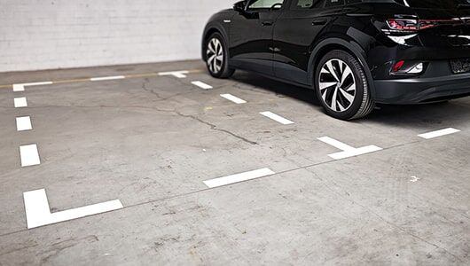 Abschnittstitelbild zur Parkplatzkennzeichnung Das Bild zeigt eine mit Fahrbahnmarkierungsfolienzuschnitten gekennzeichnete Doppelparkfläche in einem Parkhaus mit parkendem Auto