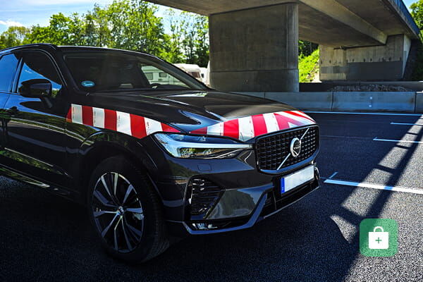 Dunkler SUV mit rot-weißer Warnmarkierung auf Motorhaube und Kotflügel.