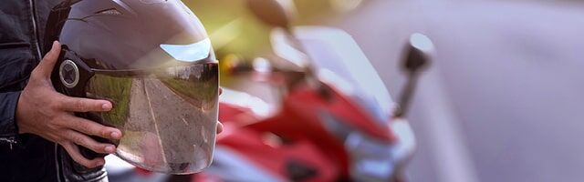 ECE Regelung 22 – Sicherheitsnorm für Motorradhelme Eine Person hält einen Helm mit Motottadhelmsticker, während im Hintergrund ein Motorrad zu sehen ist.