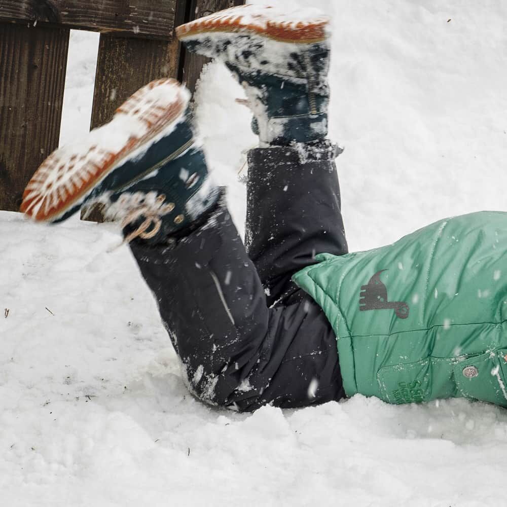 Schwarzer Dino-Bügelprint auf Kinderjacke beim Spielen im Schnee, unbeleuchtet