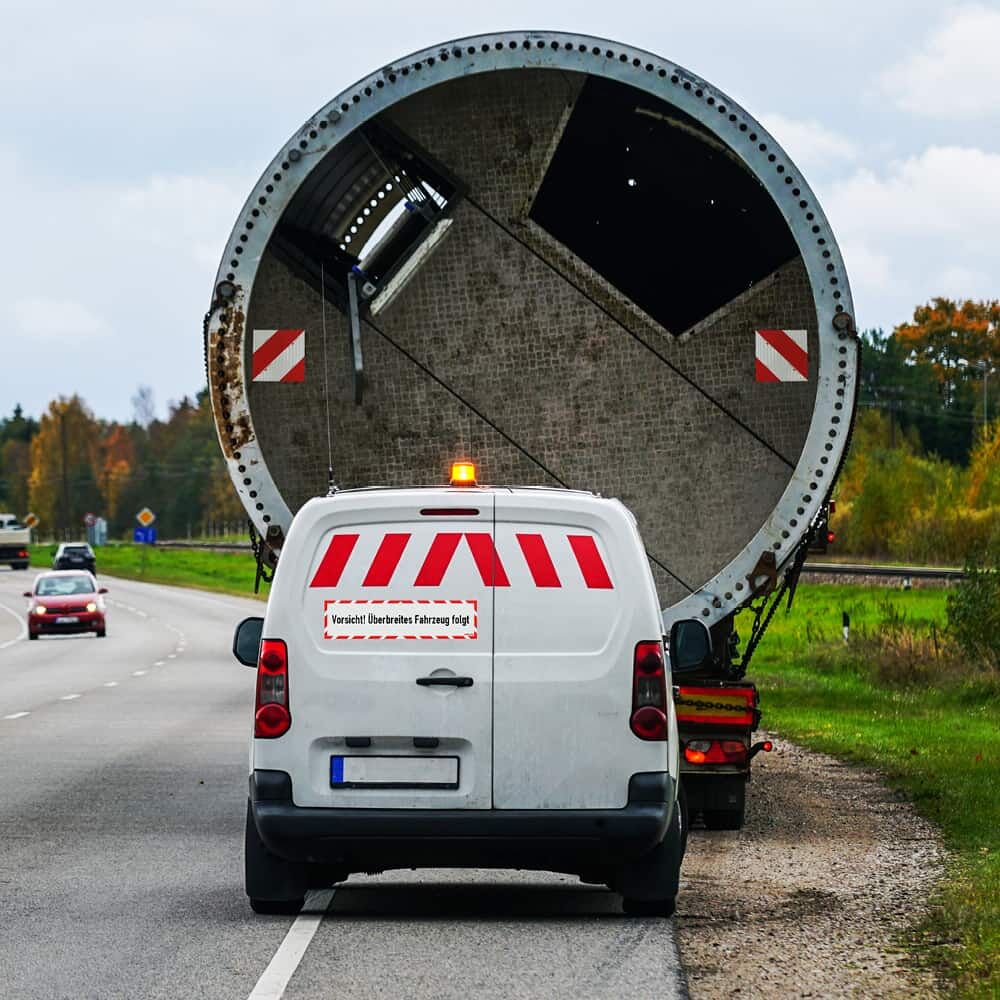 Montiertes „Vorsicht! Überbreites Fahrzeug folgt“ Hinweisschild am Heck eines Transporters