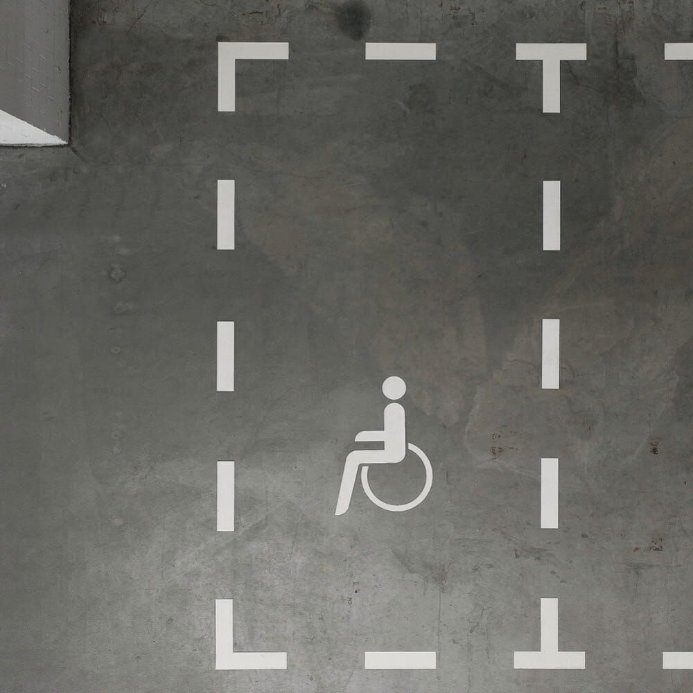 Rollstuhlsymbol als weiße Bodenmarkierung auf grauem Betonboden