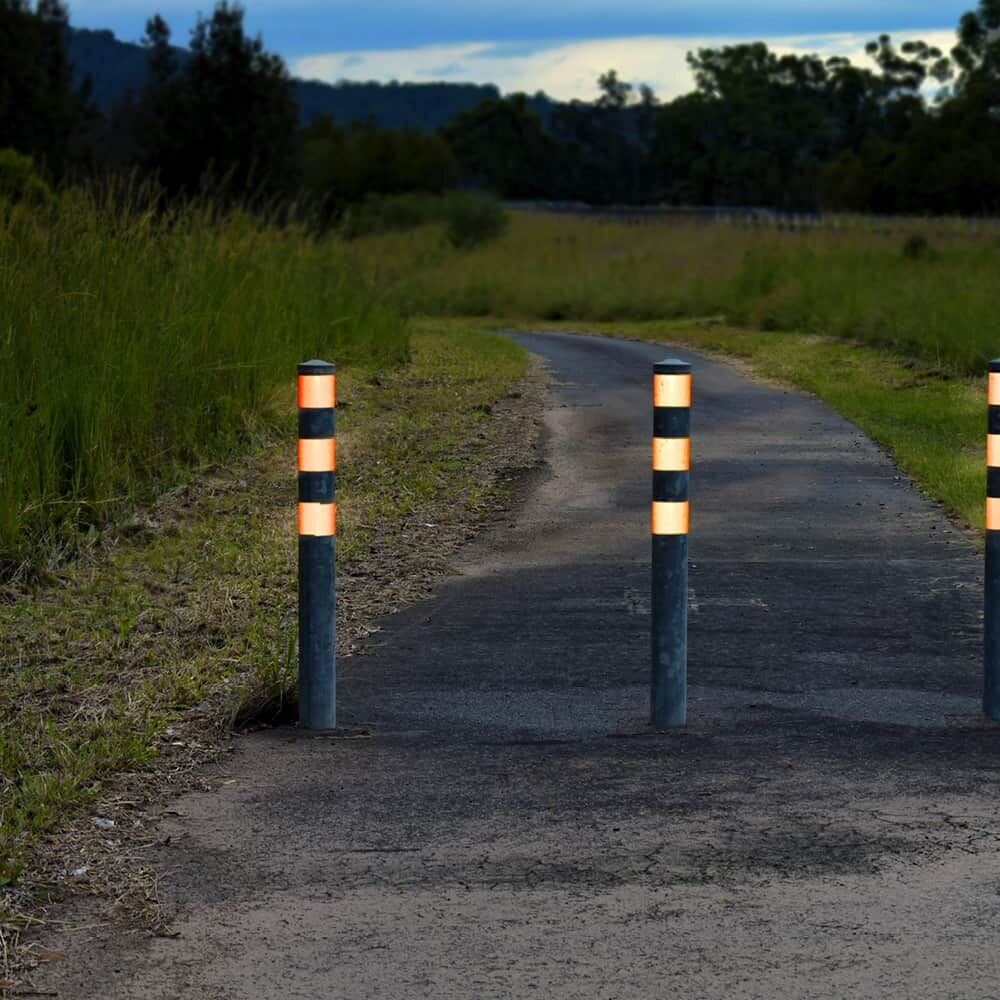 Dunkle Poller mit orange 5810-Reflexfolie leiten schmalen Weg in der Dämmerung