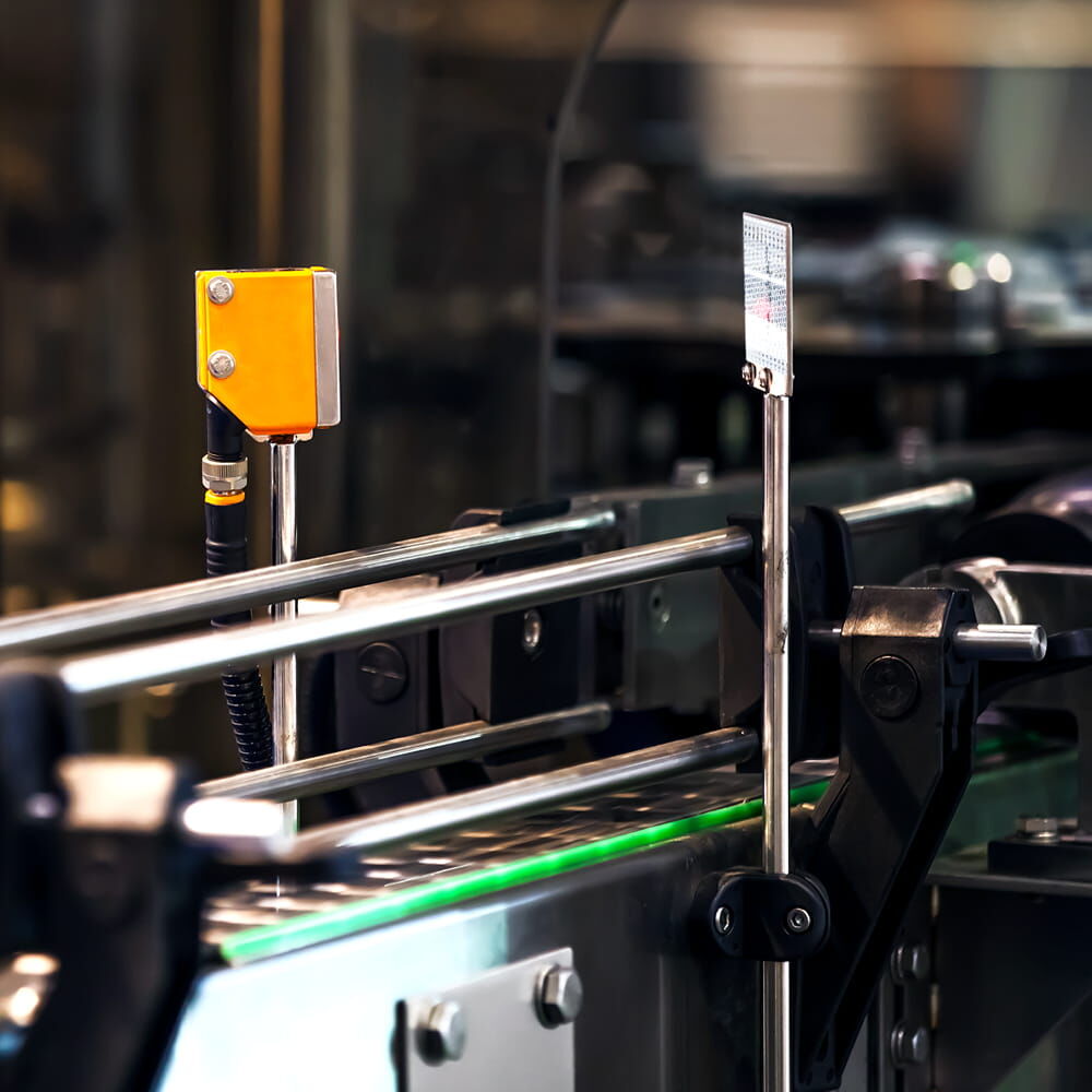 Reflektormarke Avery T-7500B an Metallstift gegenüber Lichttaster in Maschinenanlage