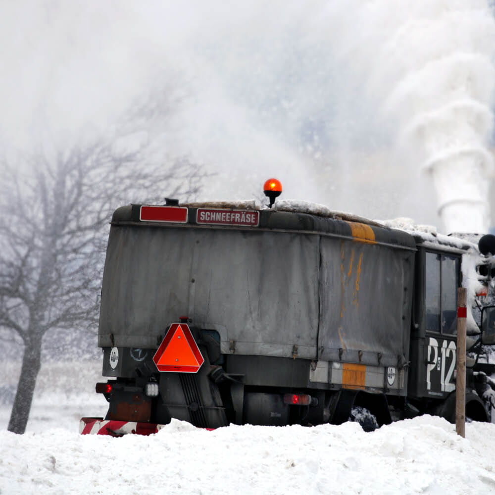 Warntafel hinten an Schneefräse im Einsatz auf verschneiter Straße