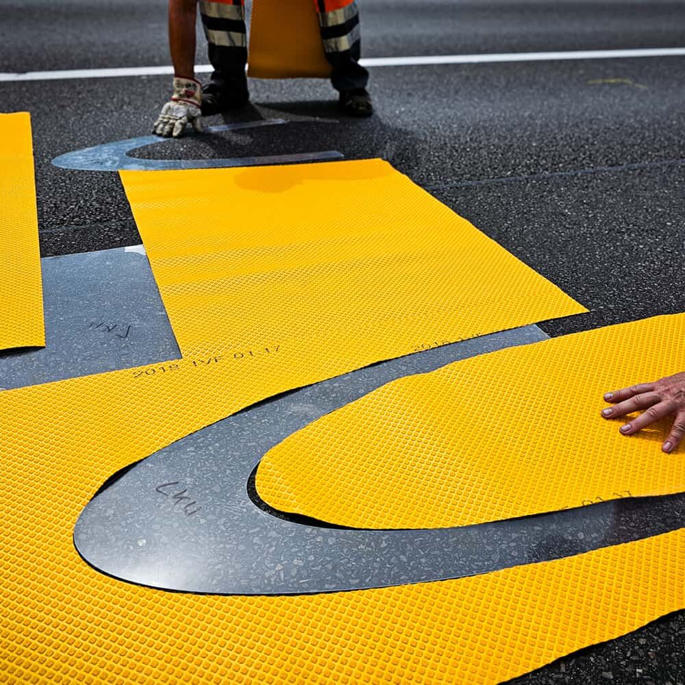 Positionierung gelber 3M Stamark Zuschnitte mithilfe von Schablonen auf Asphalt