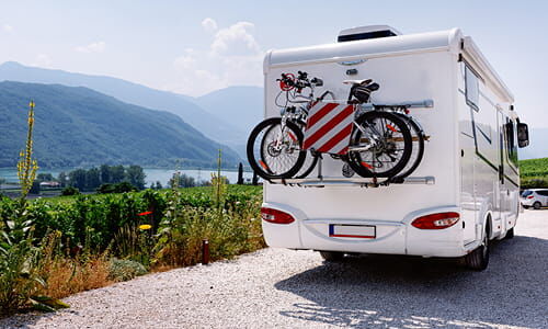 Titelbild Themenseite Caravan Das Titelbild der Themenseite Caravan zeigt ein Wohnmobil mit Fahrradaufspannung und Italientafel auf Landstraße mit See und Bergen im Hintergrund